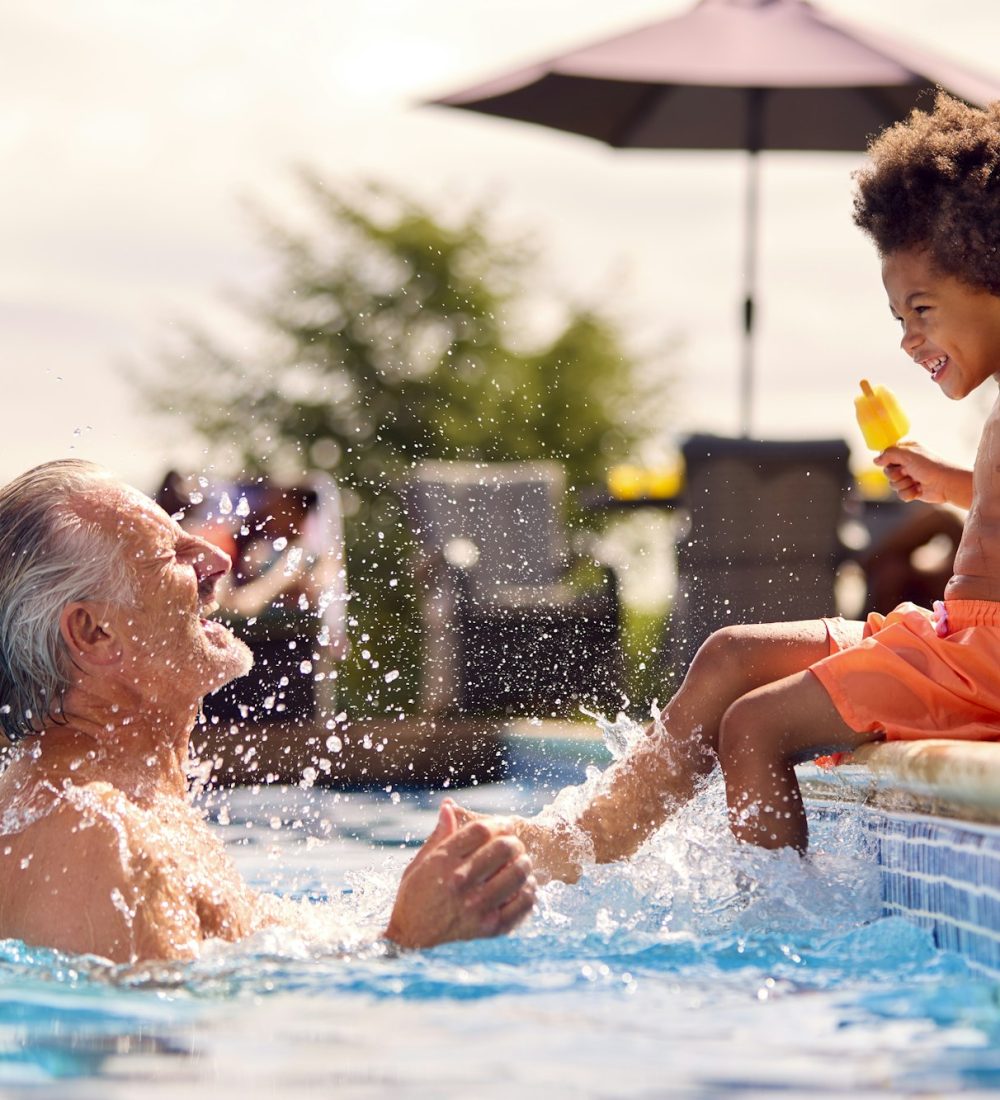 Grandfather and grandson enjoying ice cream by the pool on a sunny summer holiday